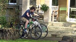 Lawrence rides two bikes from the bike shed to the front of Bath Youth Hostel